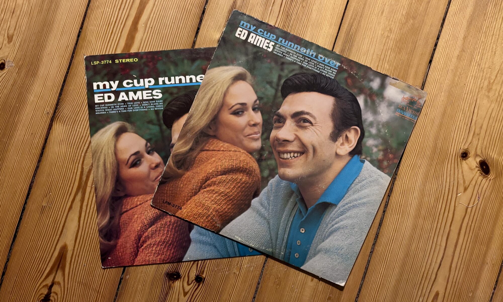 Die älteste Sache in meinem Besitz - Zwei Vintage-LP-Schallplattencover mit "My Cup Runneth Over" von Ed Ames, die jeweils Ed Ames mit einer blonden Frau zeigen, auf einer Holzoberfläche überlagert.