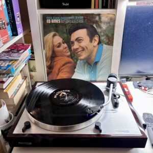 Ed Ames - my cup runneth over - Vinyl A - Eine Schallplatte auf einem Thorens-Plattenspieler, wobei das Cover "My Cup Runneth Over" von Ed Ames im Hintergrund sichtbar ist, umgeben von Bücherregalen und einem Computermonitor.