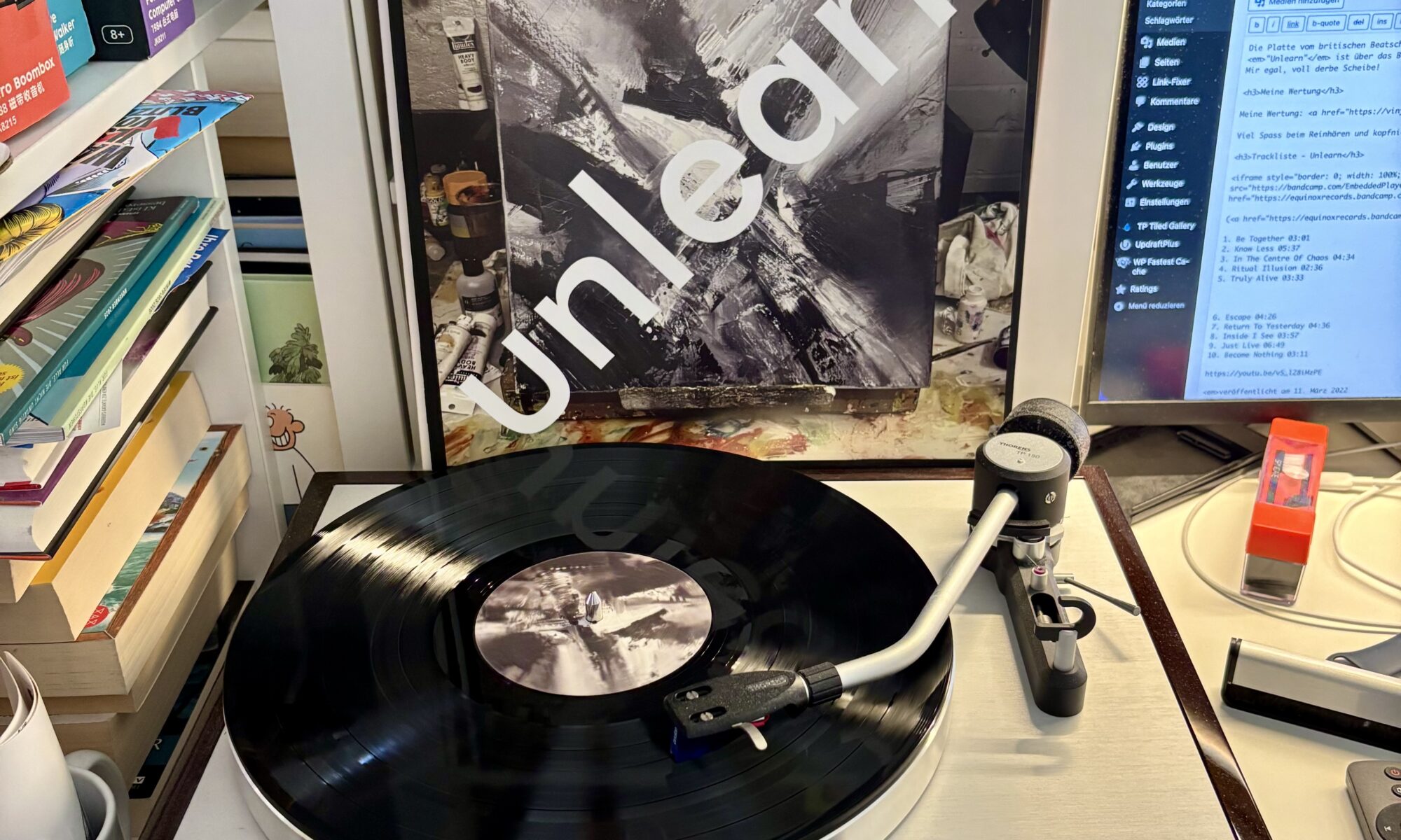 2econd class citizen unlearn vinyl a - Ein Plattenspieler mit einer schwarzen Vinyl-Schallplatte, die sich dreht, einem Schallplatten-Cover mit abstrakter Schwarz-Weiß-Kunst und dem Wort "unlearn" in Weiß aufgedruckt, und einem Computermonitor, auf dem eine Webseite angezeigt wird.